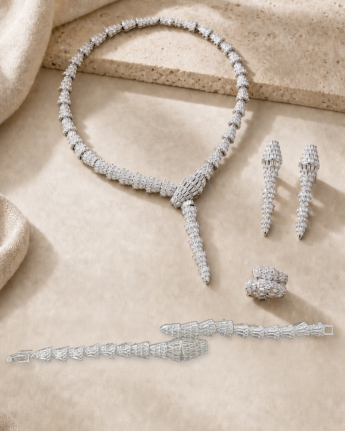 Catalogue hero of the complete Aeterna set with a silver-tone geometric Y necklace, matching long earrings, sculptural ring and articulated bracelet on warm ivory stone and linen.