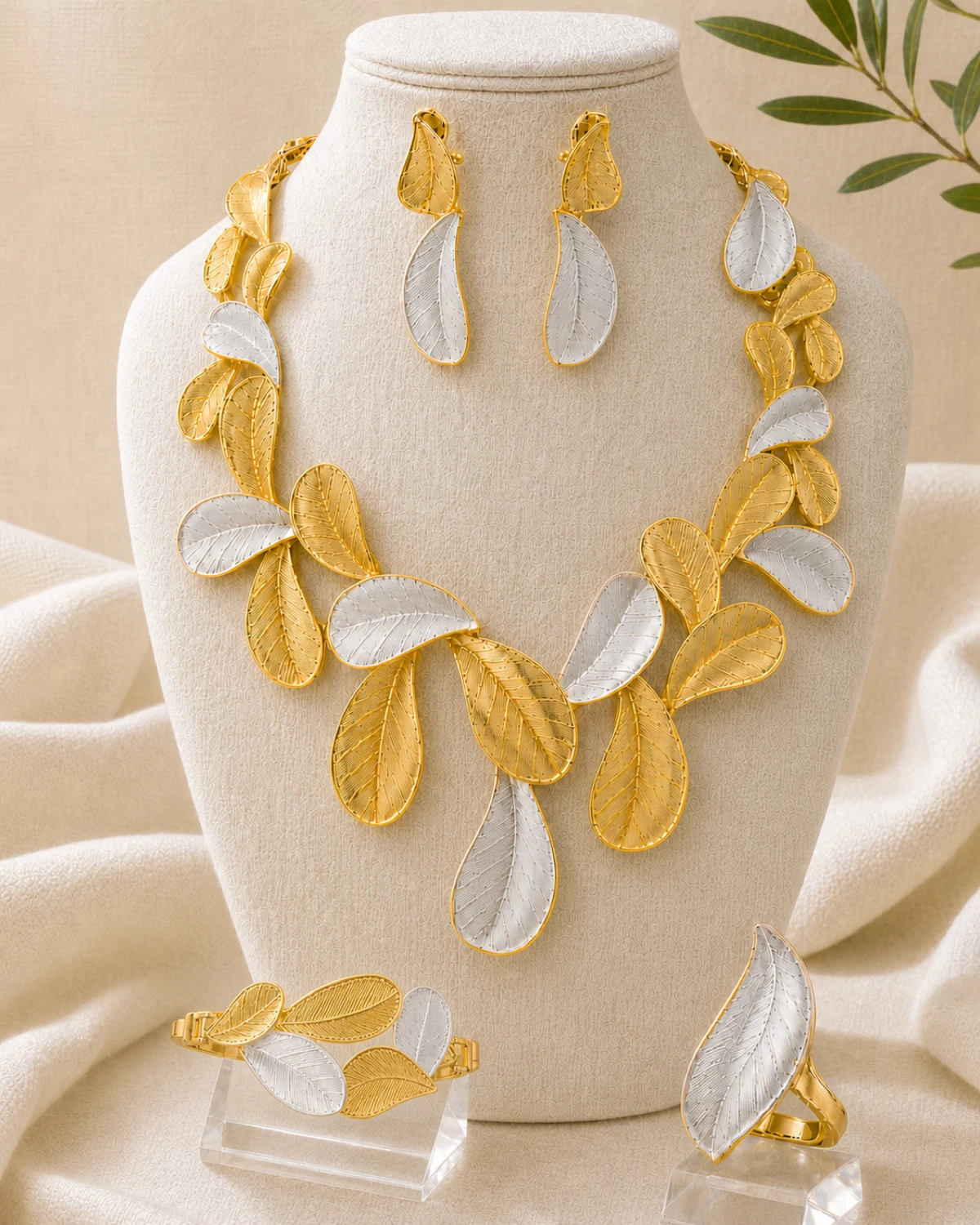 Cassia catalogue hero with the complete two-tone engraved-leaf necklace, matching earrings, bracelet and ring on a warm Linen Atelier display.