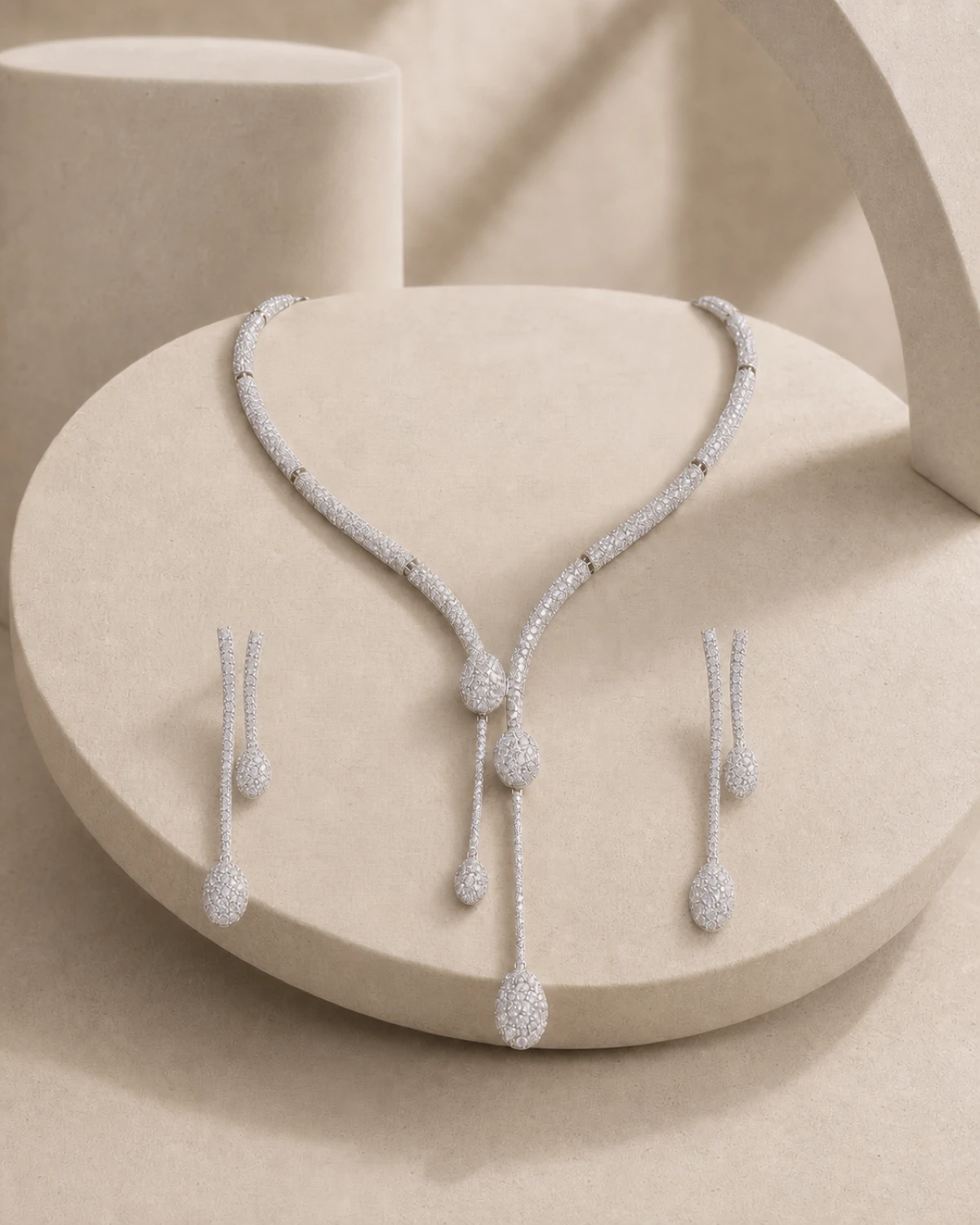 Fulgor Y necklace and matching drop earrings arranged on a pale-stone catalogue plinth.