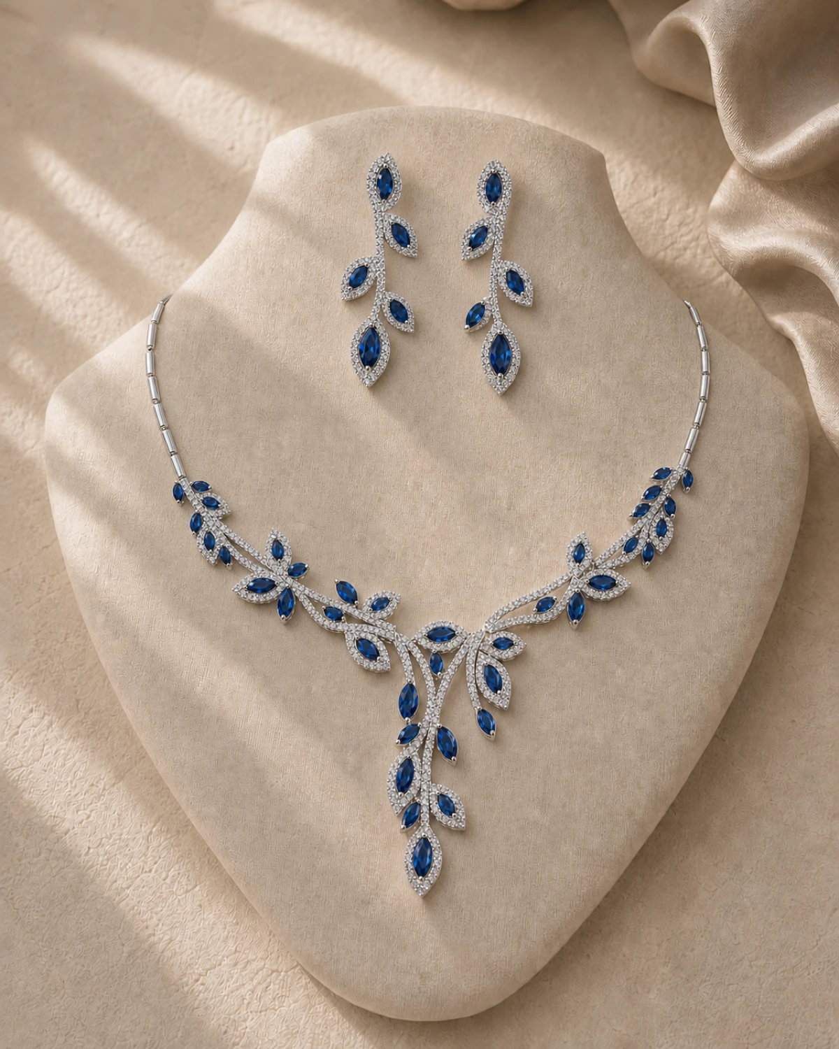 Livia silver-tone branching necklace with deep-blue marquise leaves and matching five-leaf earrings on a champagne-linen catalogue form.