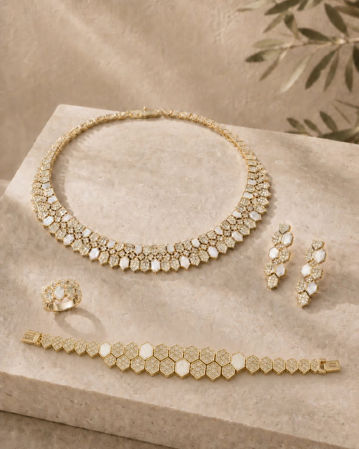 Lucilla catalogue hero on a warm stone slab, showing the polygon collar necklace, matching drop earrings, clustered ring and articulated geometric link bracelet with a dense central motif.