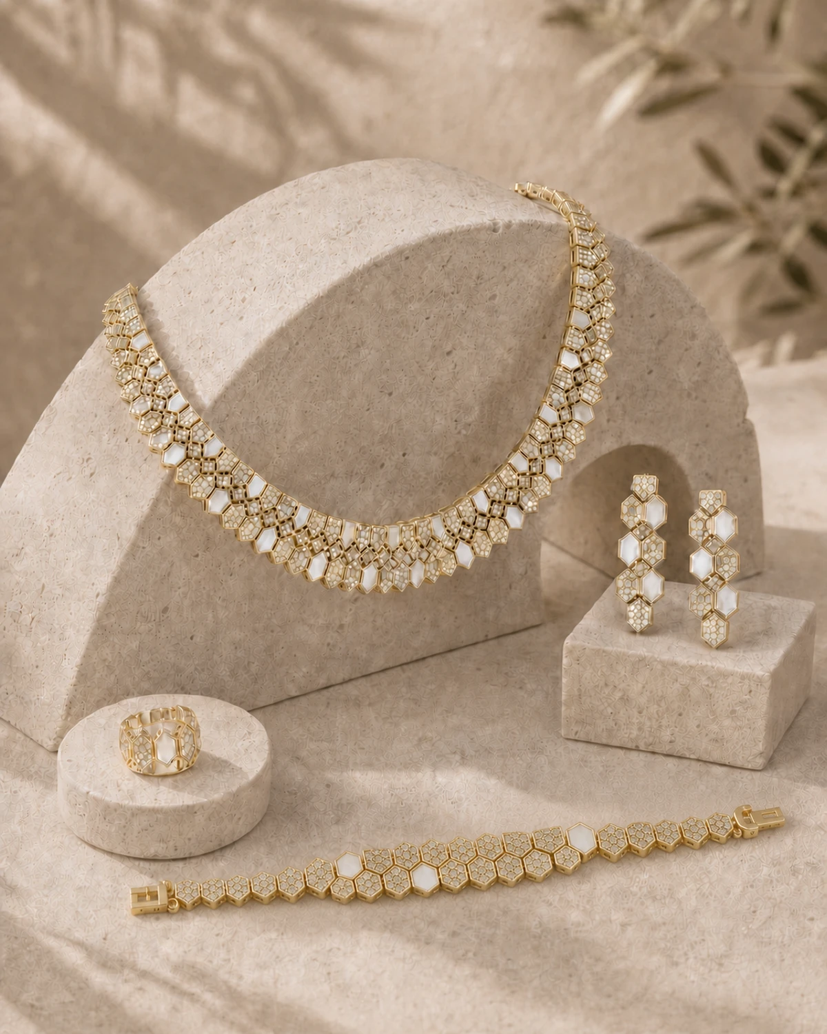 Lucilla necklace, earrings, ring and articulated geometric link bracelet displayed across sculpted pale-stone forms in soft late-morning light.