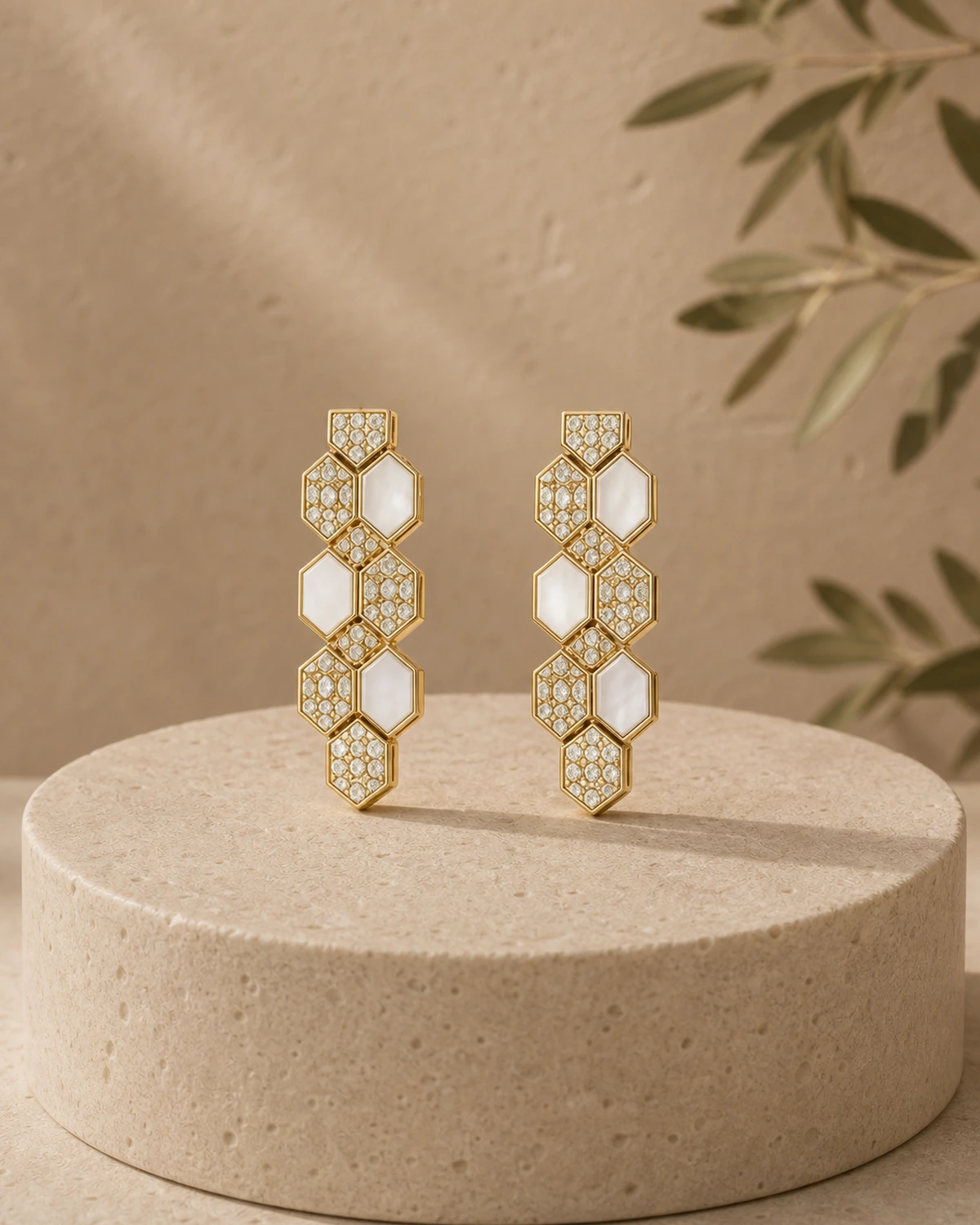 Pair of Lucilla vertical polygon-chain drop earrings on a rounded pale-stone plinth.