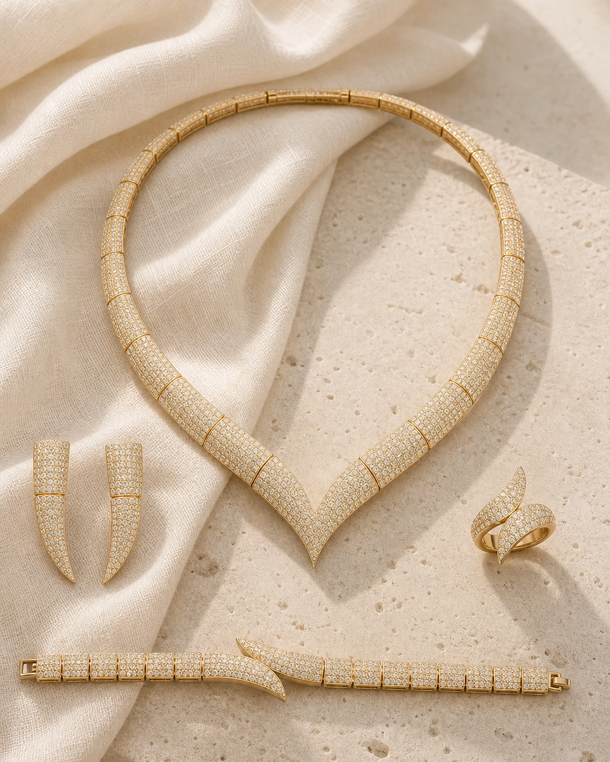 Catalogue hero of the complete five-piece Octavia set with one segmented warm-gold-tone V collar, two curved earrings, one overlapping-curve ring and one rectangular-link bracelet on ivory linen and pale stone.