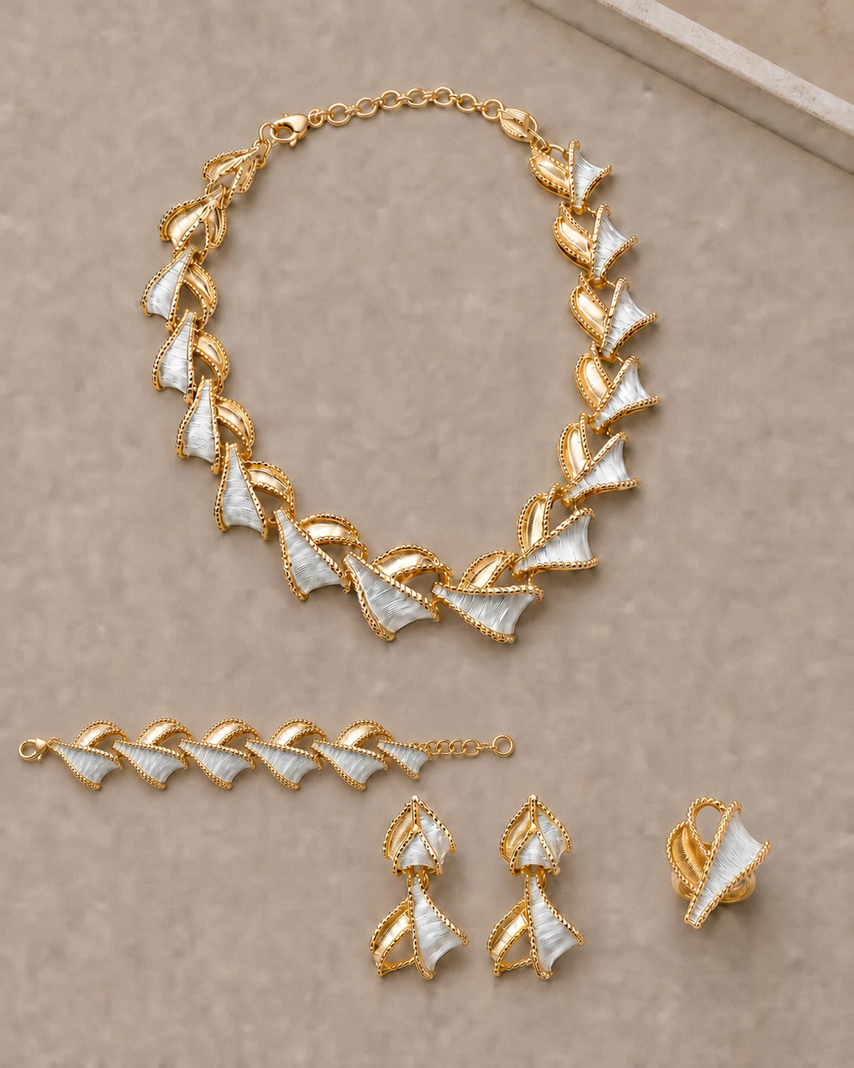 Overhead full-set view of the Vesper necklace, matching earring pair, compact ring and bracelet arranged separately on a warm-taupe surface.