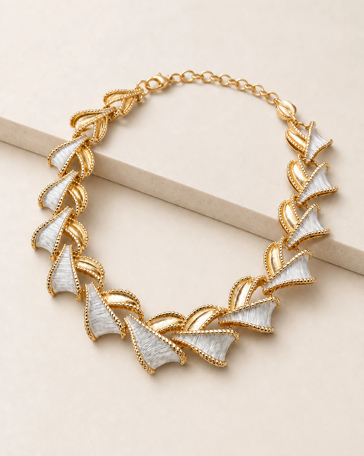 Close product view of the complete Vesper necklace showing alternating warm-tone ribbed leaf forms and pale satin-fan forms with beaded warm-tone edges.